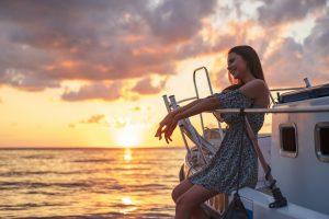 Young attractive woman sitting on the deck of yacht and enjoying sunset